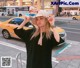 A woman in a black dress and a white hat is standing on the street.