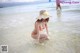 A woman in an orange bikini and a straw hat in the water.