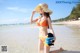 A woman in a bikini and hat holding a stuffed animal on the beach.