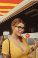 A woman in a yellow dress and glasses standing in front of a food truck.