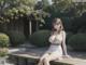 A woman in a white dress sitting on a wooden bench.